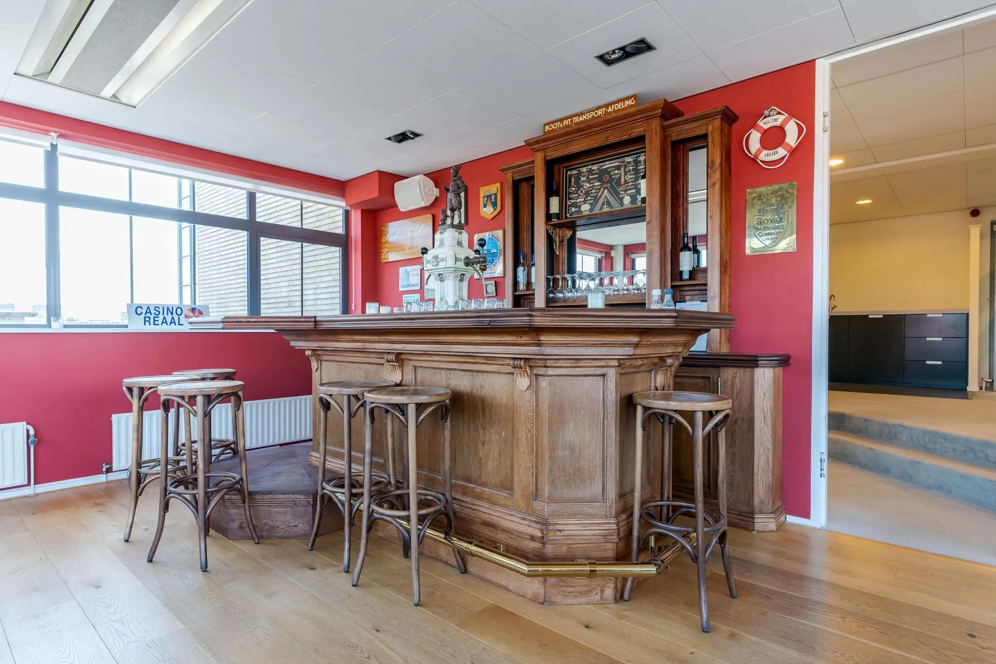 Houten bar met krukken in een ruimte aan de Van Alkemadelaan, met rode muren en decoratieve elementen.